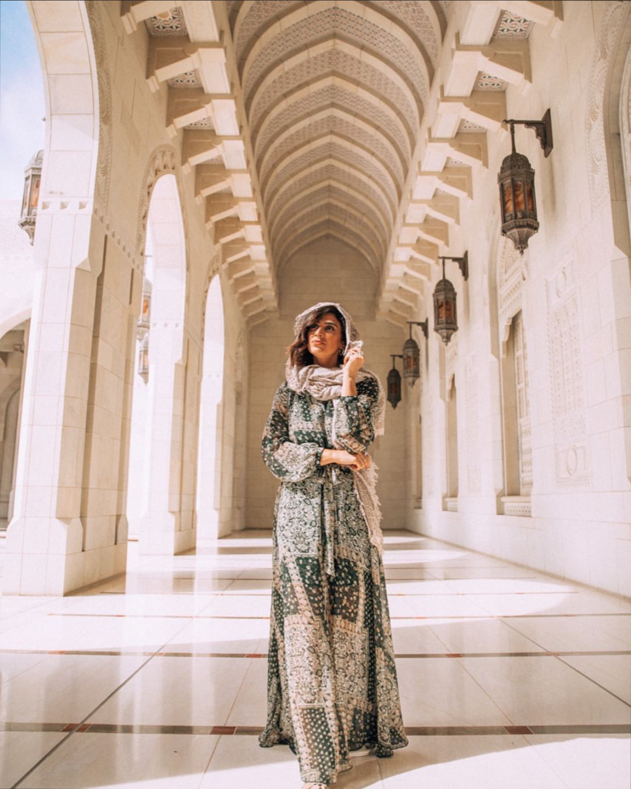 Girl posing in the hallway of Sultan Qaboos Grand Mosque, Oman wearing a long dress and head scarf