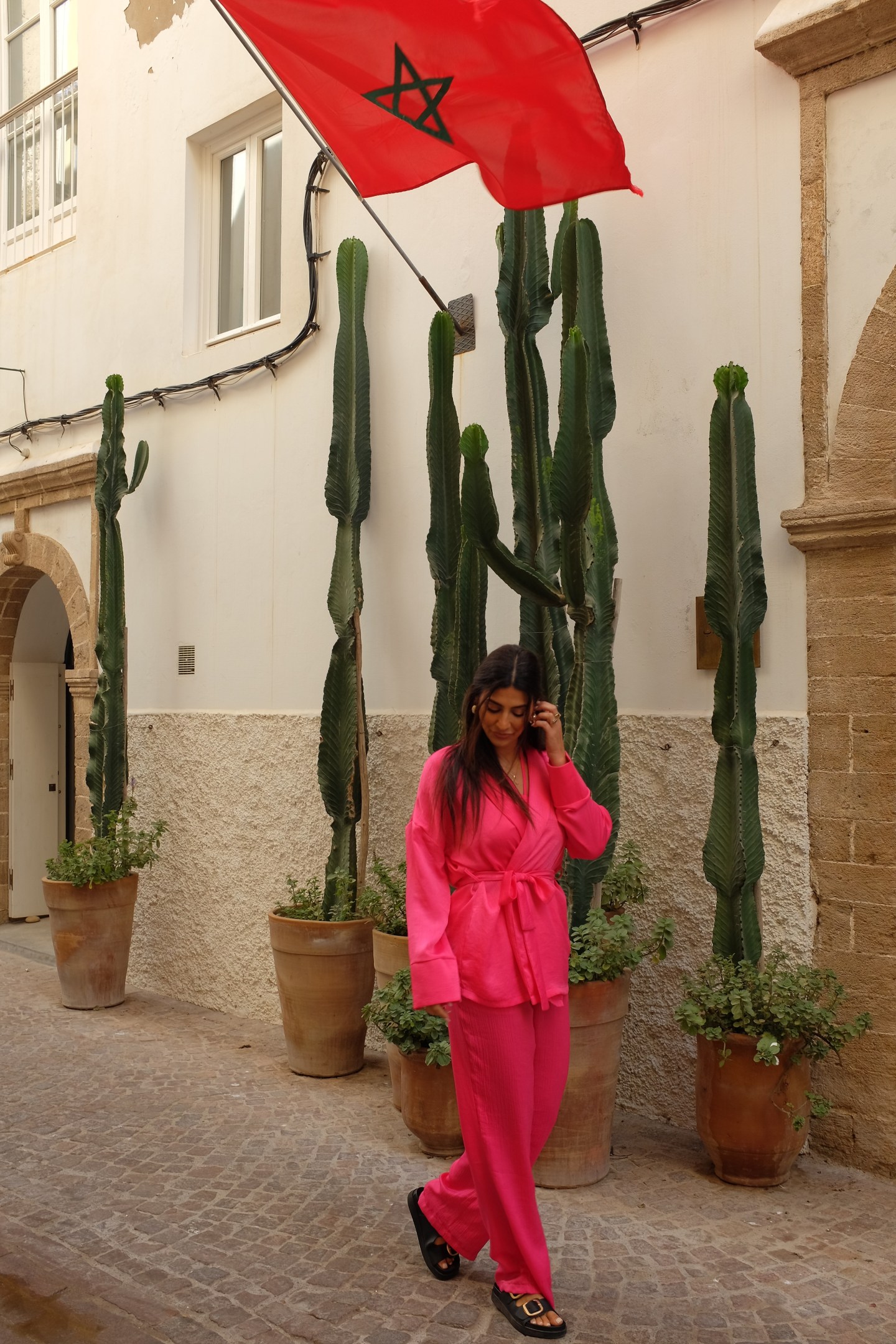 Girl wandering the streets in a pink set with Moroccan flag waving above her